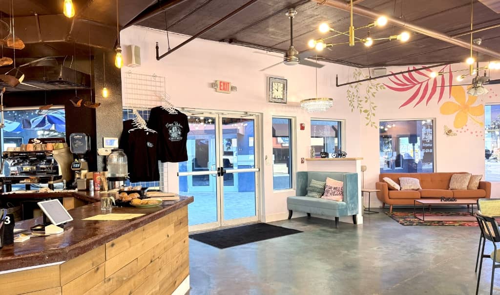 indoor coffee shop with concrete floors, wood front counter, white walls painted with flowers, and a brown leather couch