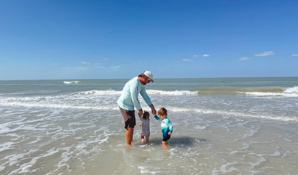 father with two toddlers at the beach playing in the waves on a sunny day in florida