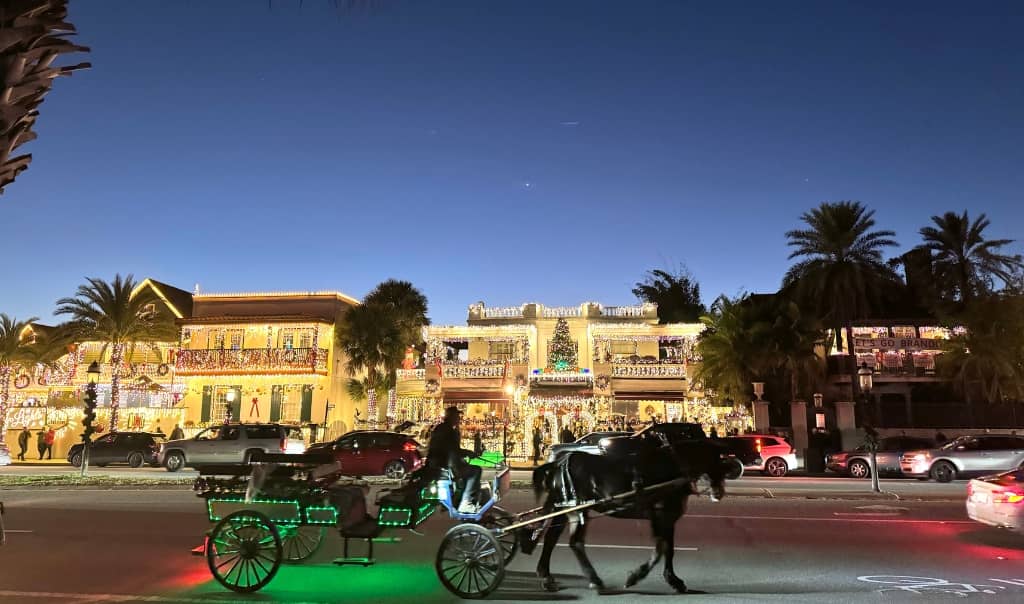 horse drawn carriage riding by lit up historic homes covered in christmas lights
