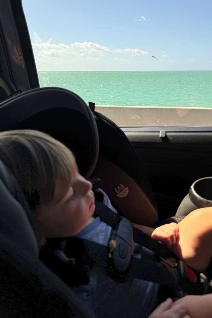 toddler sleeping in his car seat with the turquoise water of the florida keys in the background