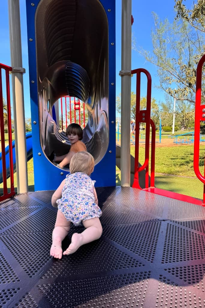 two toddlers playing on a playground with an enclosed tube section 