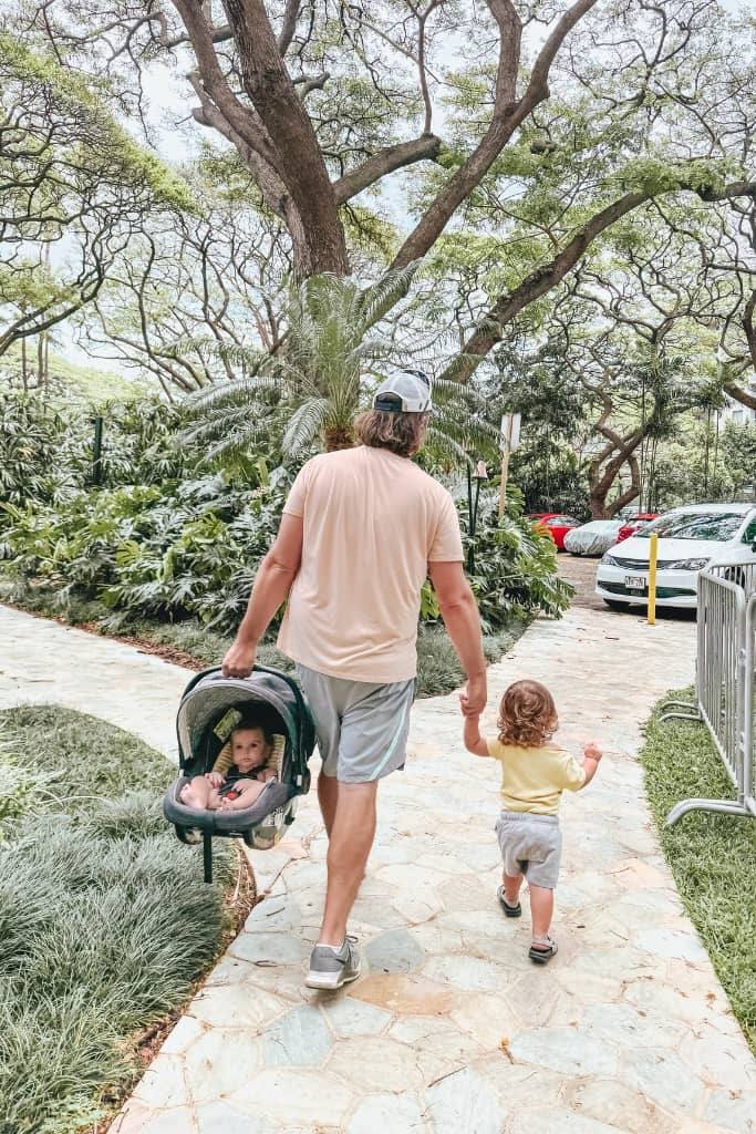 dad holding a toddlers hand and carrying a baby in an infant seat 