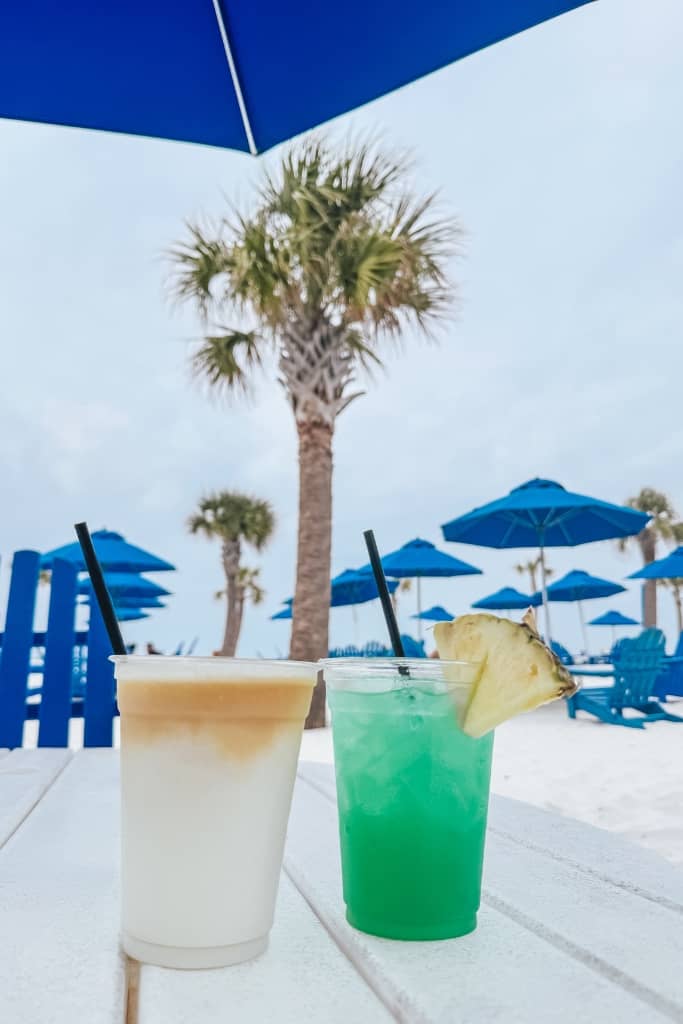 two drinks at a tiki bar on the beach surrounded by palm trees 