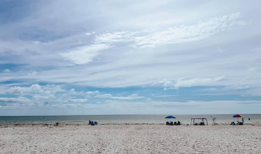 blue skies with some clouds on the beach with some umbrellas and beach chairs