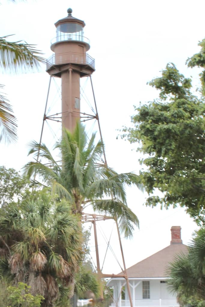 brown lighthouse surrounded by palm trees and a historic white building