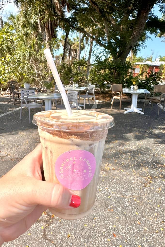 holding coffee with whipped cream in front of outdoor seating and tropical trees