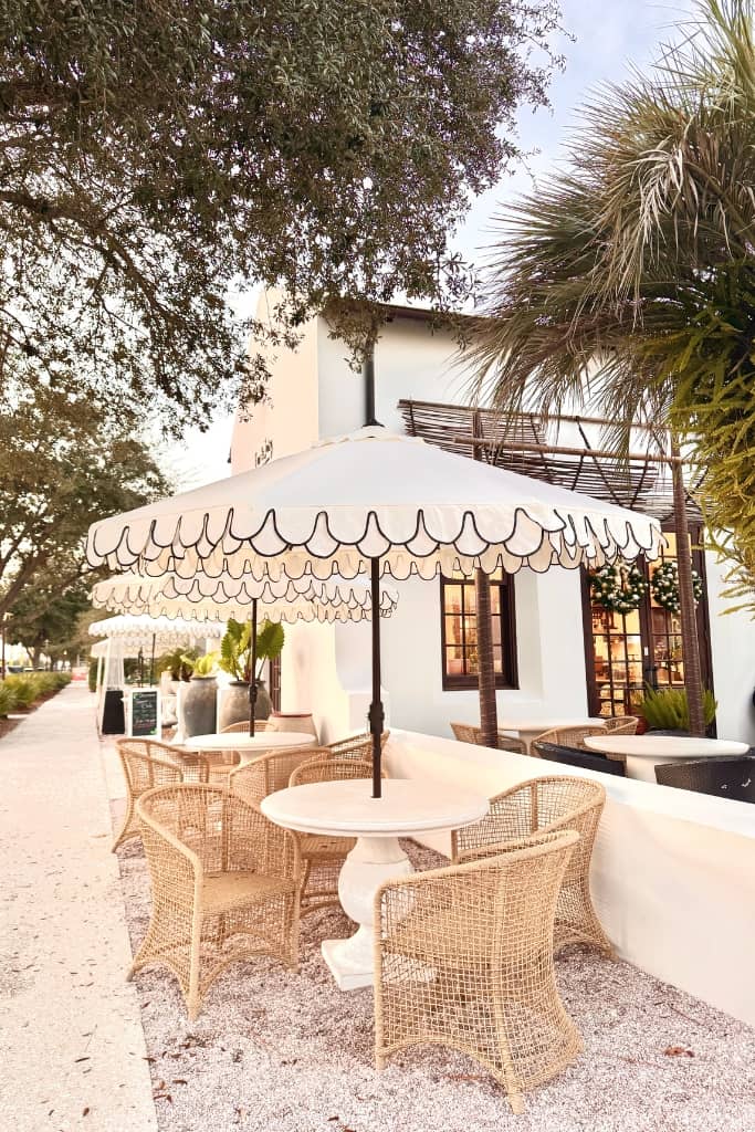 white umbrella with rattan seats on the sidewalk in front of a restaurant