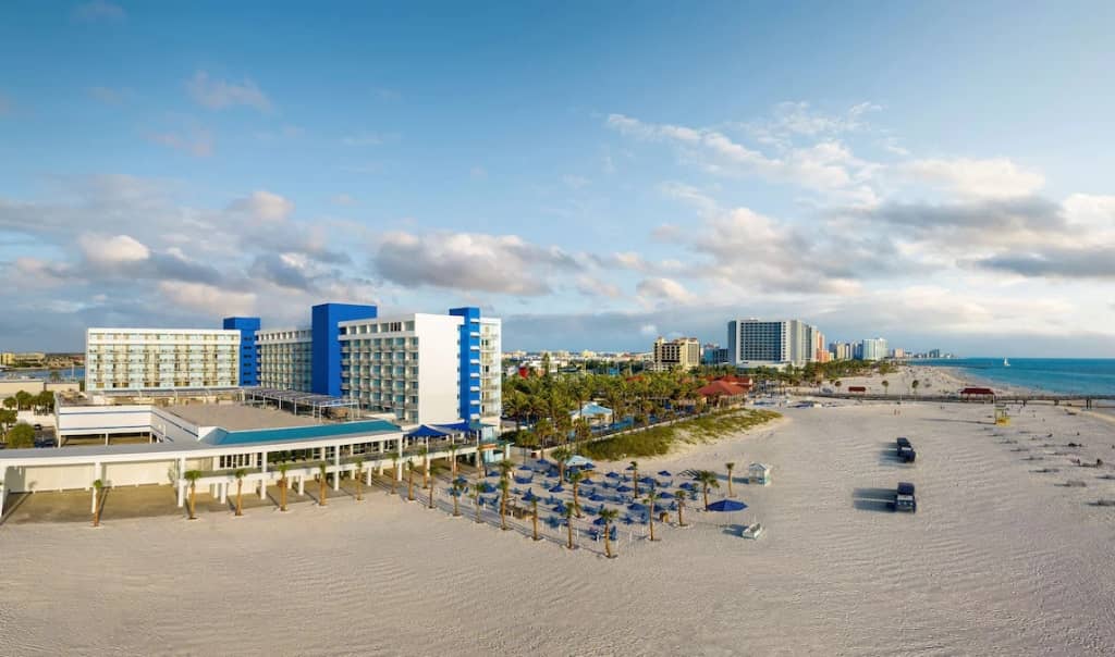 view of hilton clearwater beach showing the whole building sitting on the beach with a pool and beach chairs and beach umbrellas