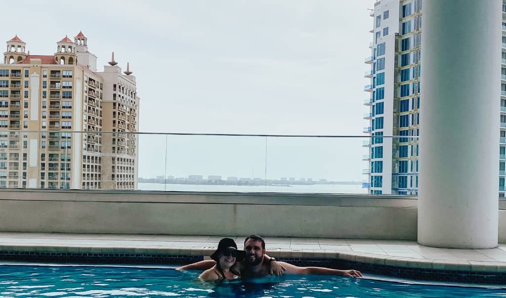 couple posing in a rooftop pool with buildings in downtown sarasota in the background