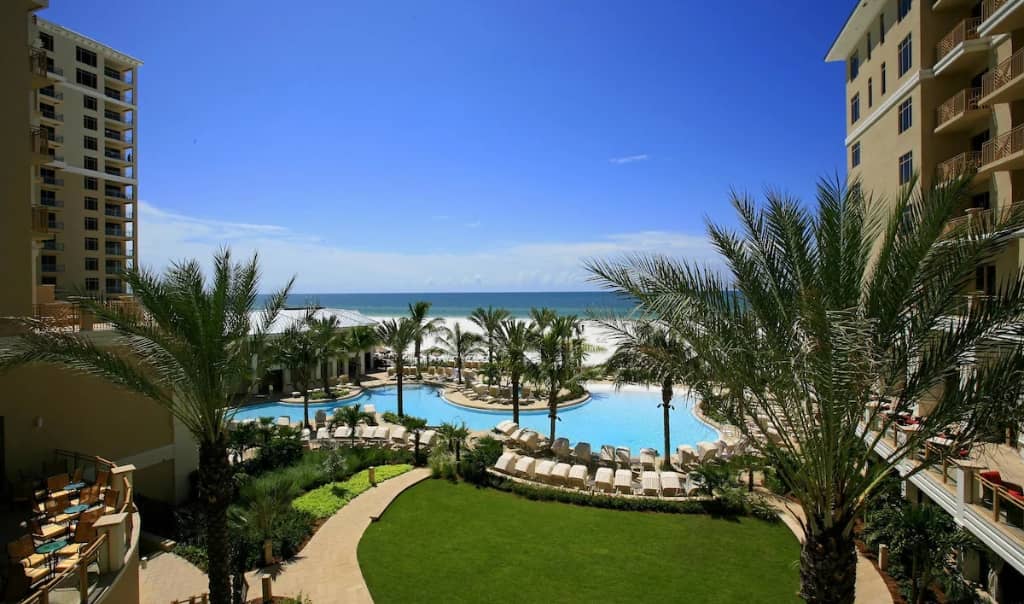 palm trees, artificial grass, and resort pool overlooking clearwater beach on a sunny day