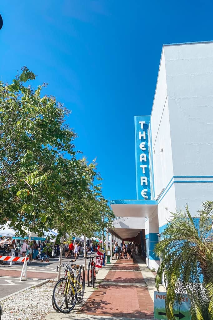 bikes parked in a bike rack with a large theatre and a vintage theatre sign in blue along the street. on the street there is a farmers market with tons of vendors and visitors in florida