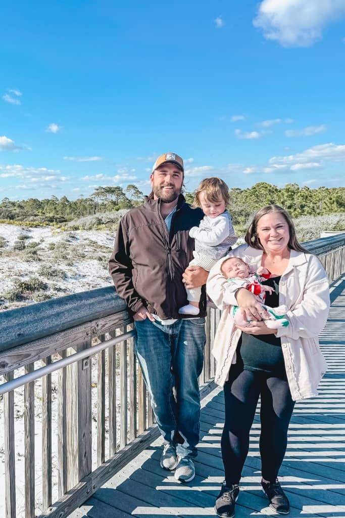 mom, dad, baby, and toddler on the boardwalk with sand dunes in the background at topsail hill preserve state park