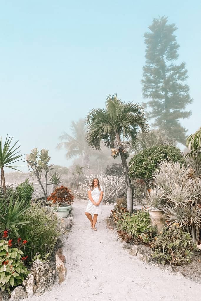 girl posing on a gravel path along a secret garden with tons of tropical foliage on a foggy day near the beach in florida