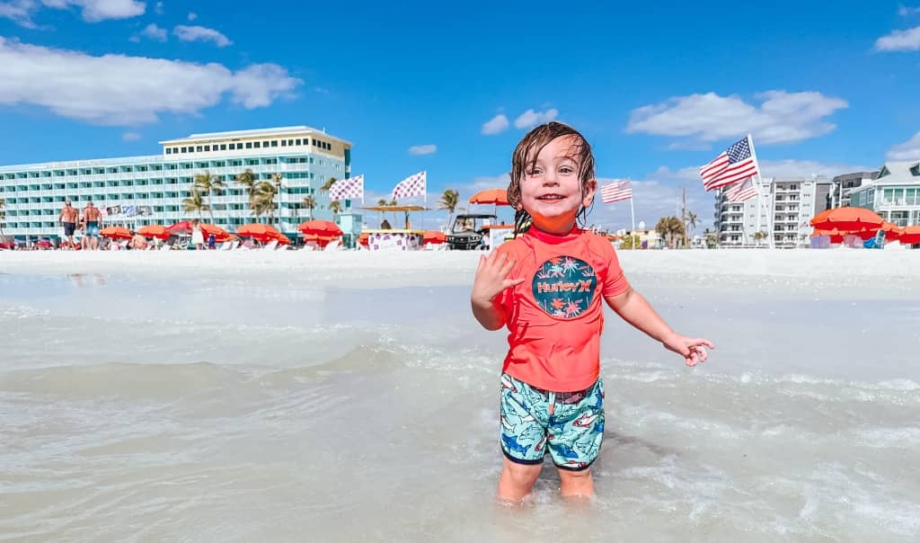 toddler in a swimsuit at the beach on a sunny day in front of the lani kai resort in fort myers beach
