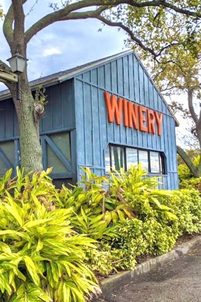 large blue building with winery in large orange letters and tropical foliage