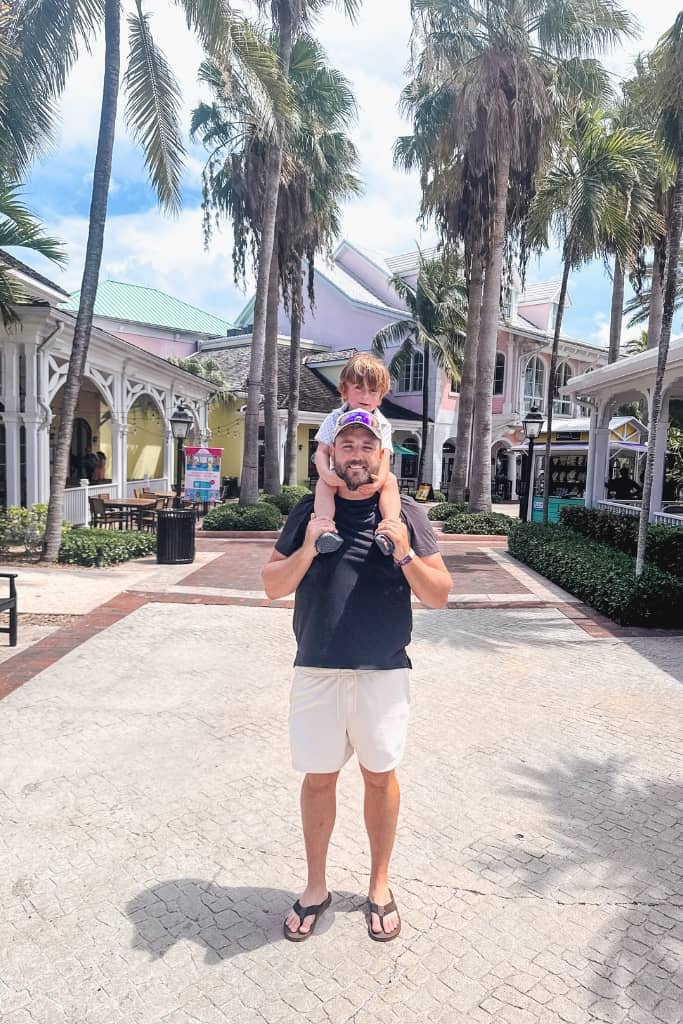 dad holding 2 year old on his shoulders with palm trees lining a sidewalk in harbor village in nassau 