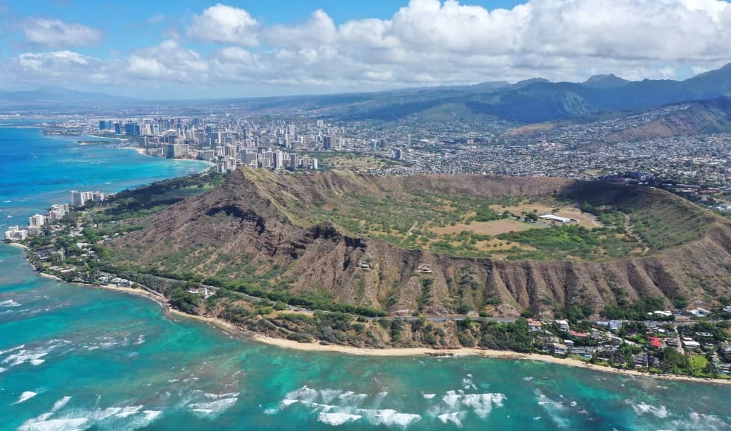 diamond head taken from an airplane with the city of honlulu in the background and ocean meeting the coastline of oahu