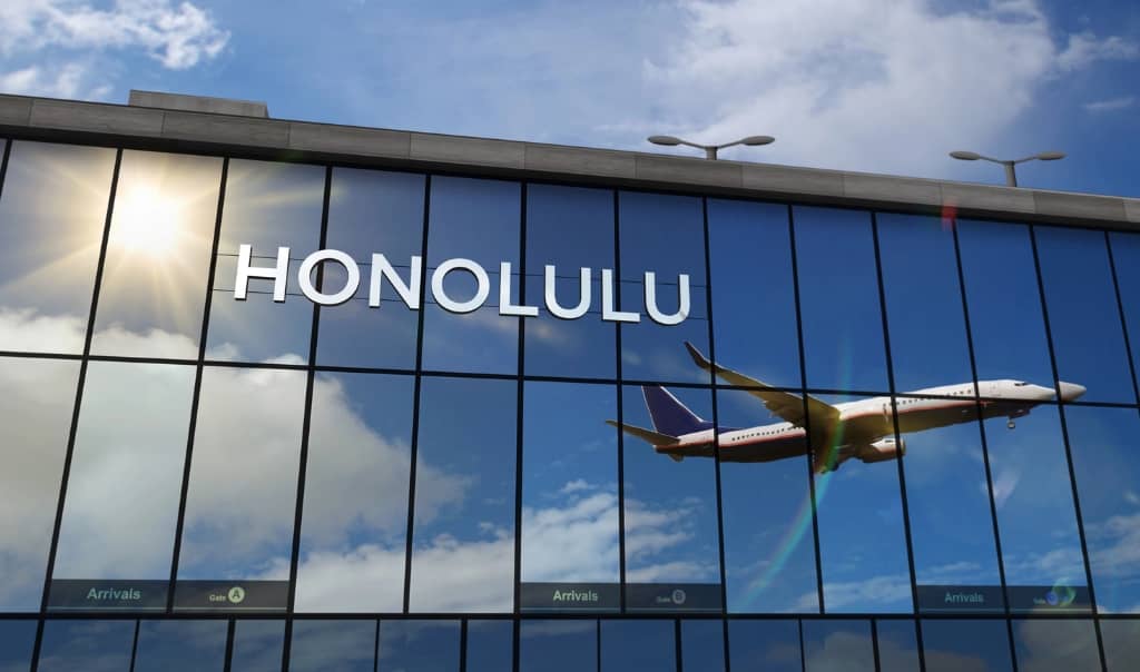 reflection of a flight taking off from the airport from a glass building that says honolulu on the building