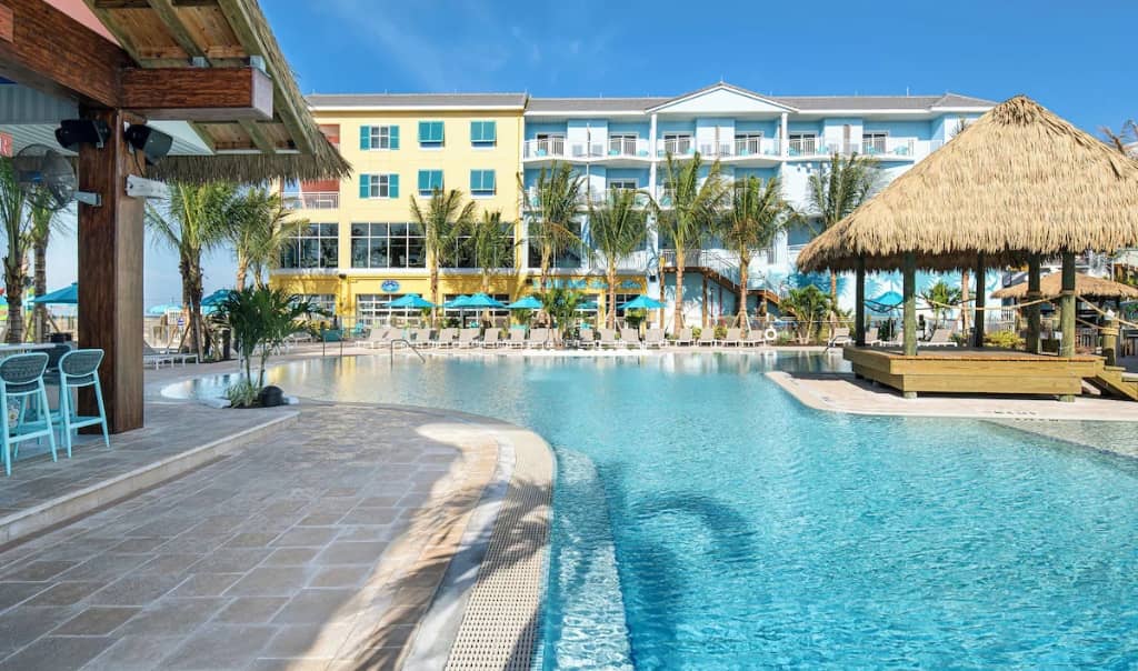 large pool surrounded by palm trees, a tiki hut, and a large resort