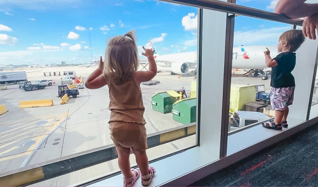 boy and girl toddler standing in airport window looking at the planes on the airport tarmac