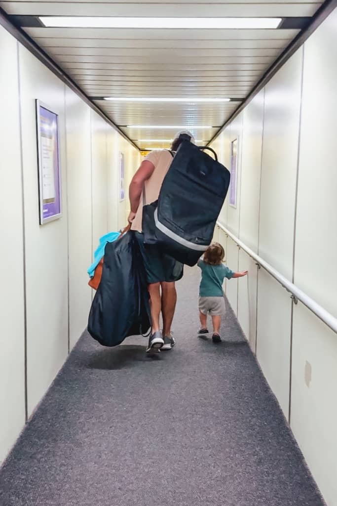 dad carrying several bags and holding his toddlers hand on the airplane jet bridge at the airport
