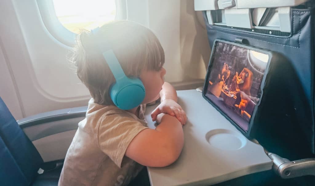 toddler boy wearing headphones and watching a movie on an ipad on an airplane