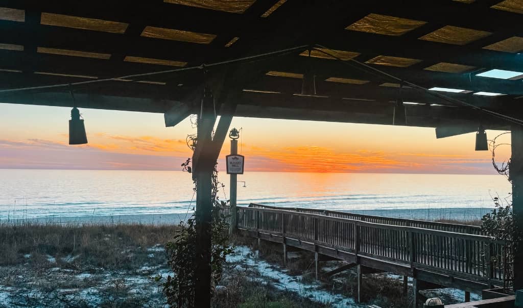 beachfront restaurant during sunset with trail to the beach in the background and several wooden restaurant booths