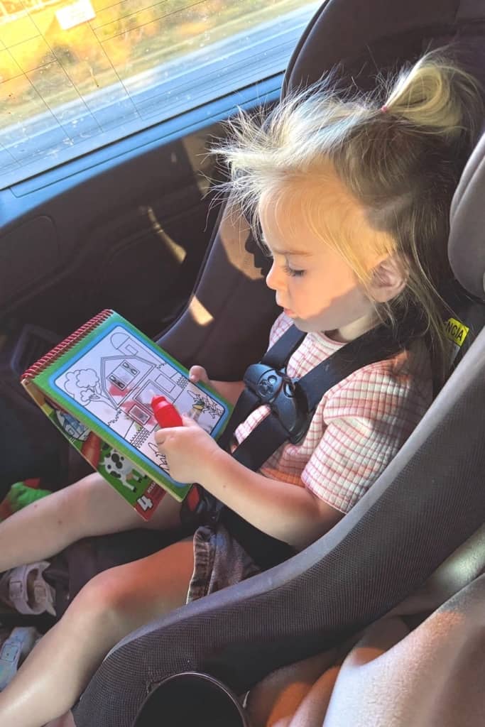 toddler playing with an activity book in her car seat on a road trip