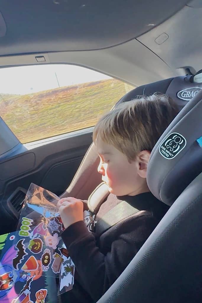 toddler playing with stickers in his car seat on a road trip