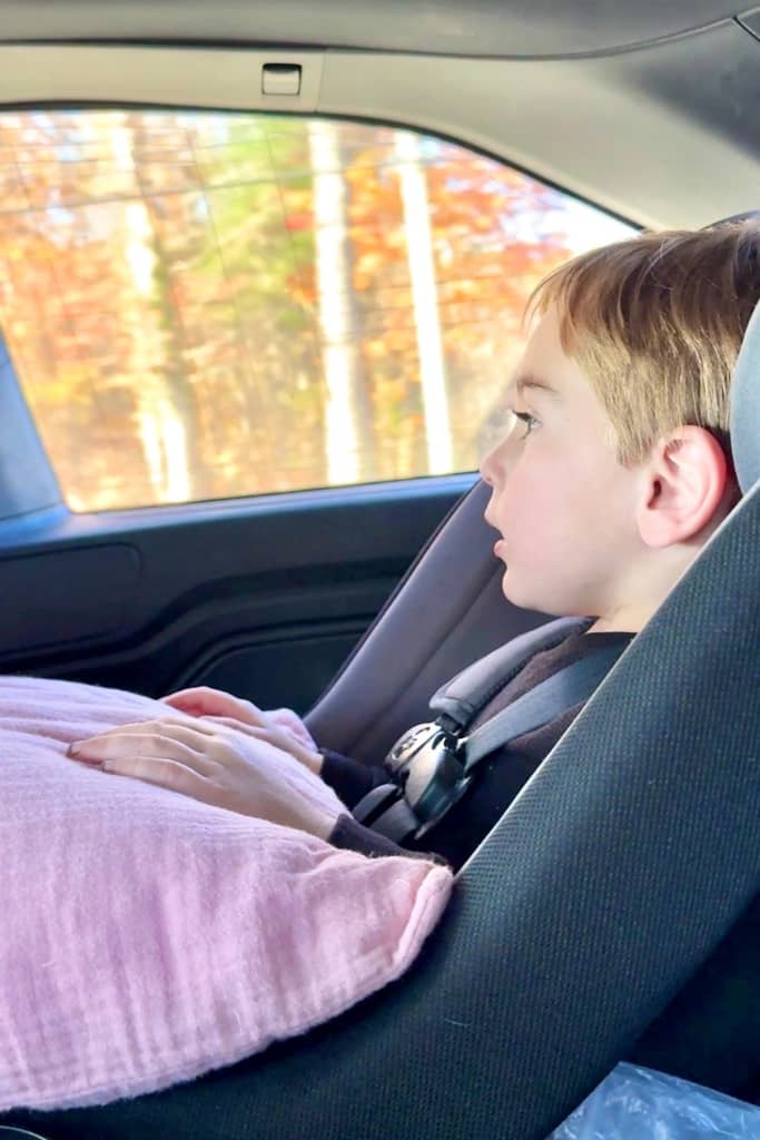 toddler holding a pillow looking out the window at fall leaves on a road trip