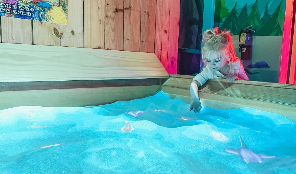 toddler girl playing in an interactive exhibit with sand