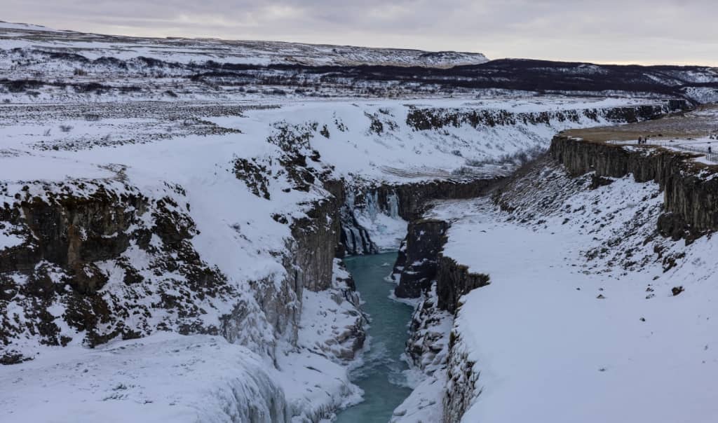 moss-covered cliffs covered in snow with a winding river running in between them and dramatic green canyon walls