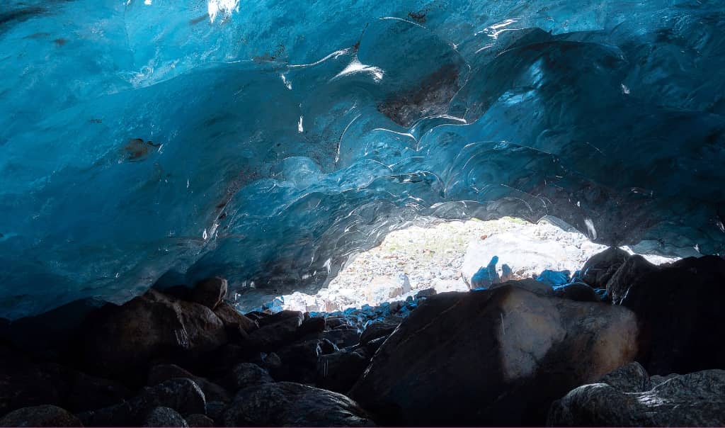 dramatic Icelandic ice cave, with vivid blue glacier ice forming curved walls and a tunnel-like opening.