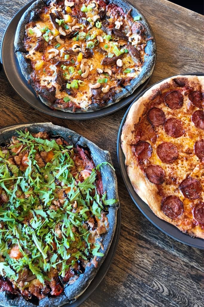 picture of three pizzas, two with black crust and one with regular crust
