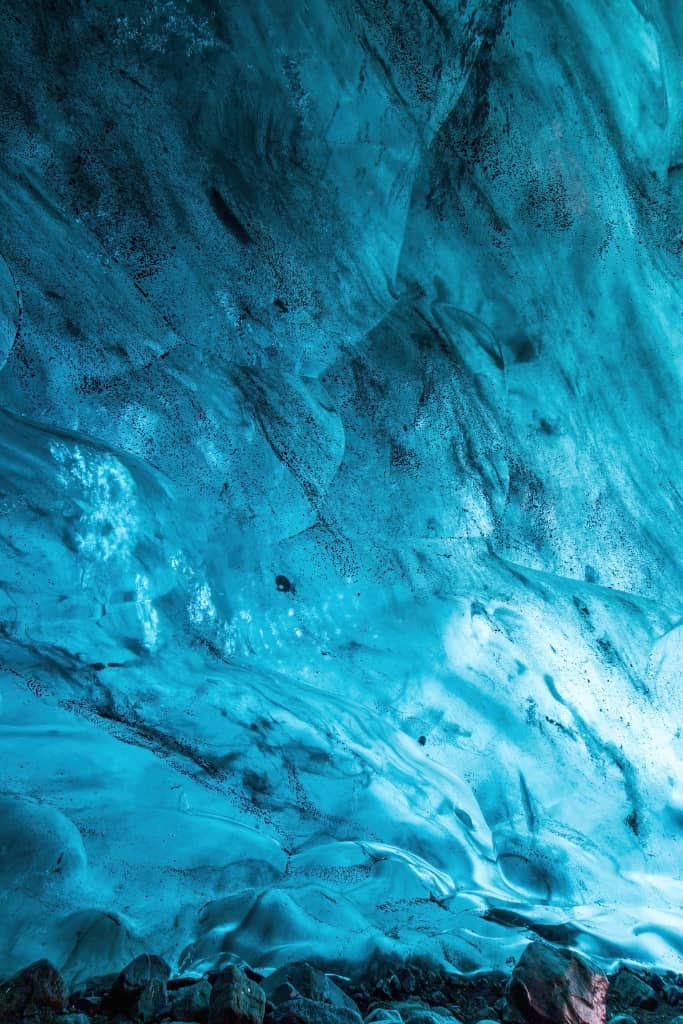dramatic Icelandic ice cave, with vivid blue glacier ice forming curved walls and a tunnel-like opening.
