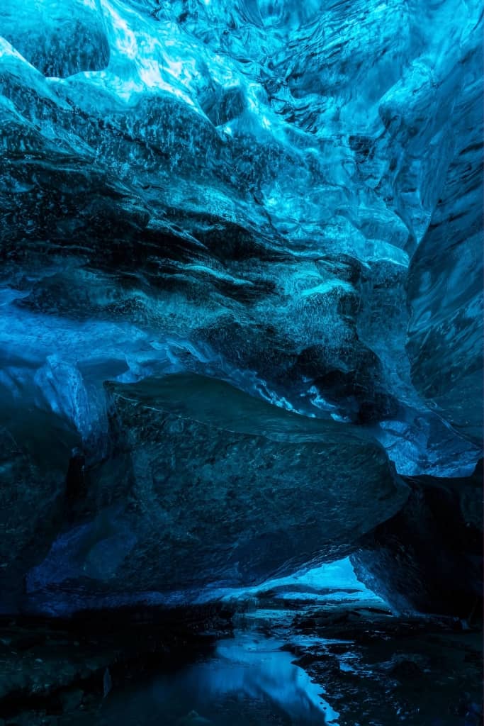 dramatic Icelandic ice cave, with vivid blue glacier ice forming curved walls and a tunnel-like opening.